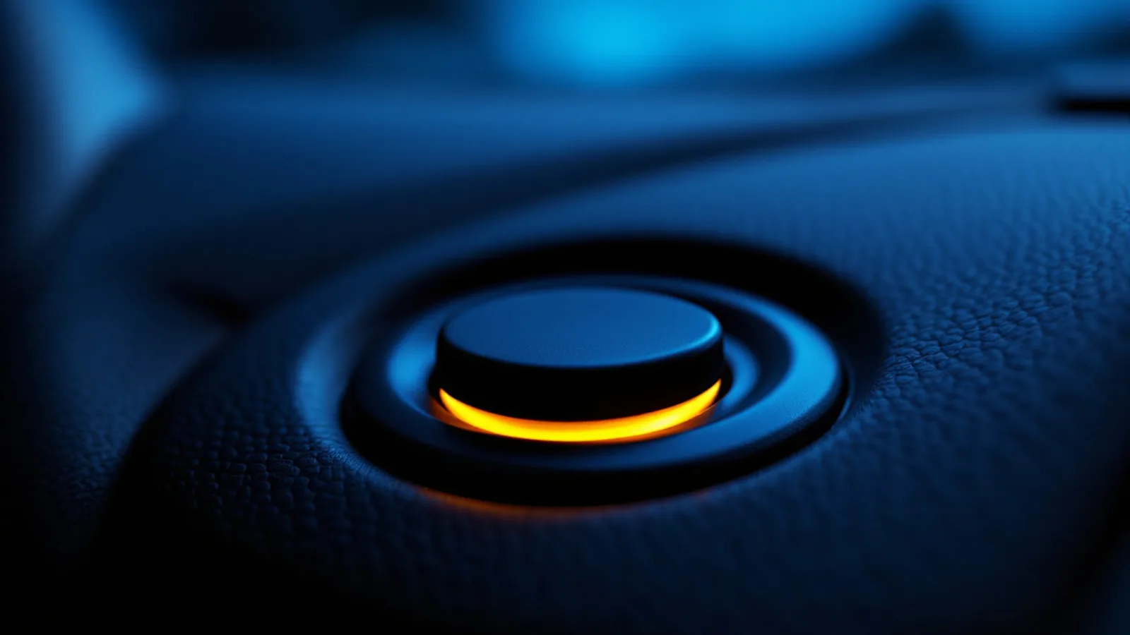 A push-button ignition switch glowing amber on a dark leather dashboard in dim blue evening light